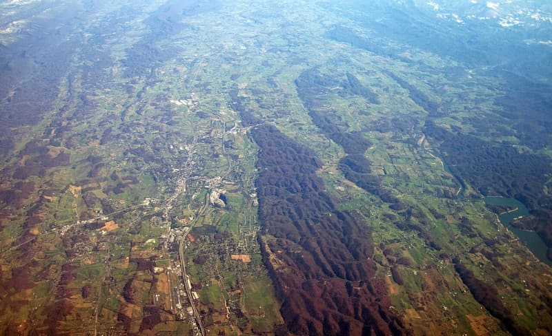 Aerial view of long wooded ridges with farmland and a town in the valleys between them, in late autumn