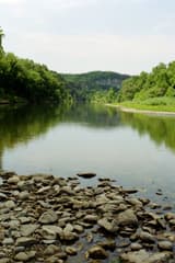 Clear, still river with a bar of pale gravel and cobbles in front, wooded banks and a rock bluff behind