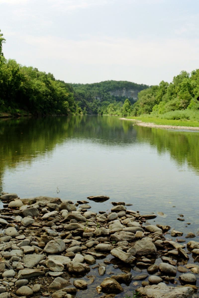 Clear, still river with a bar of pale gravel and cobbles in front, wooded banks and a rock bluff behind